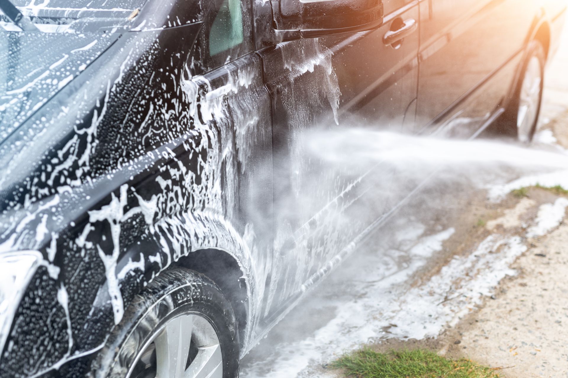 Black car being washed with foamy soap and a water hose.