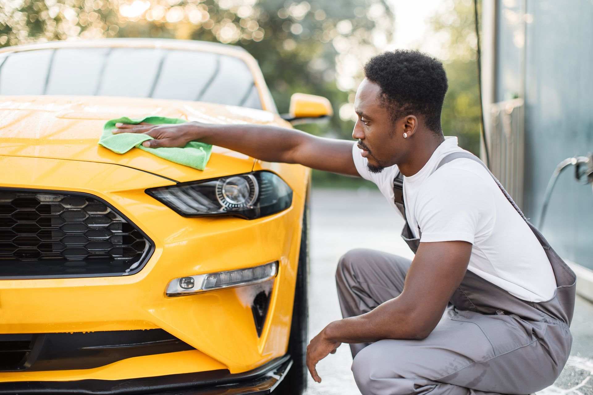 Man wiping the hood of a yellow car with a green cloth.