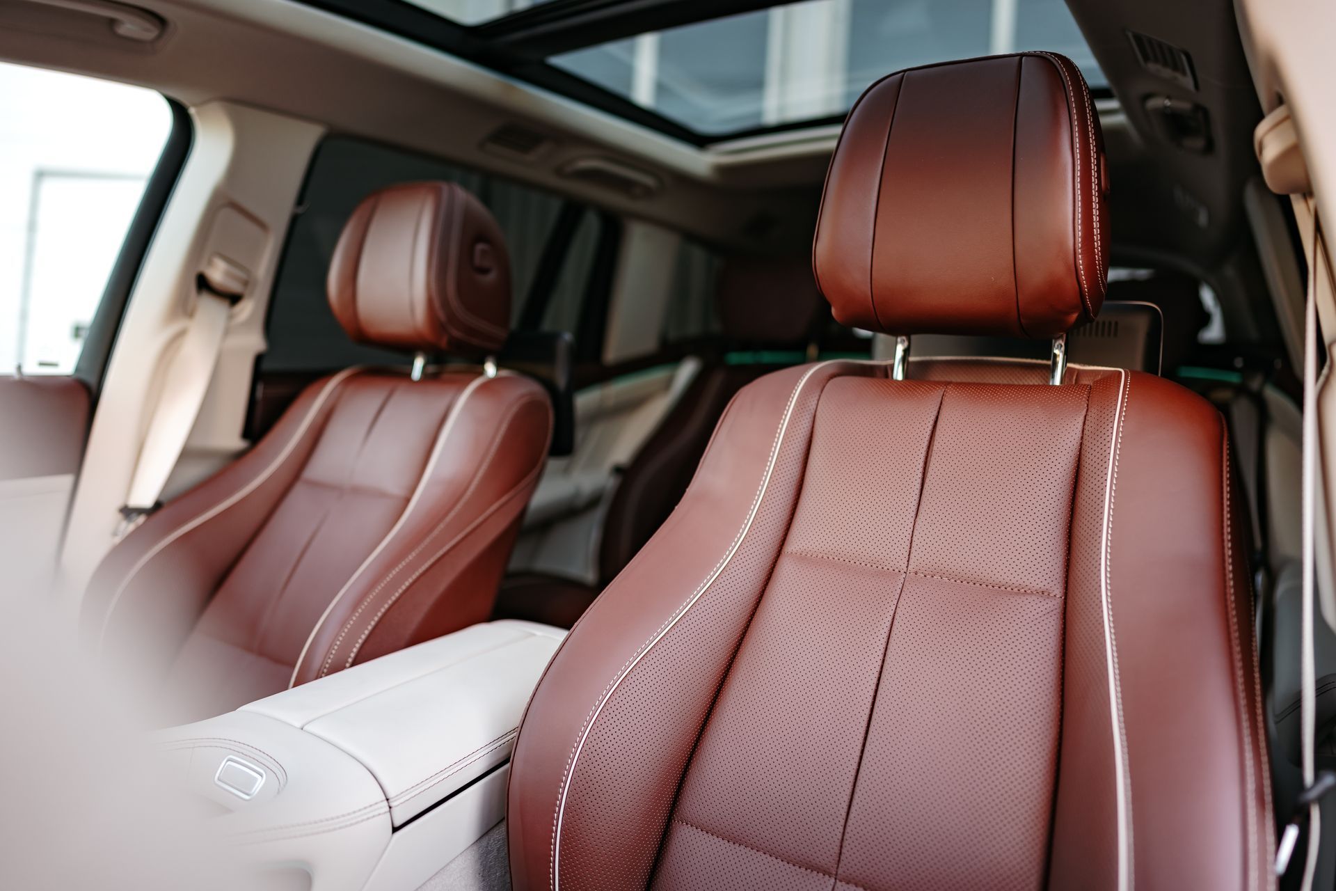 Brown leather car seats with white stitching and a sunroof.