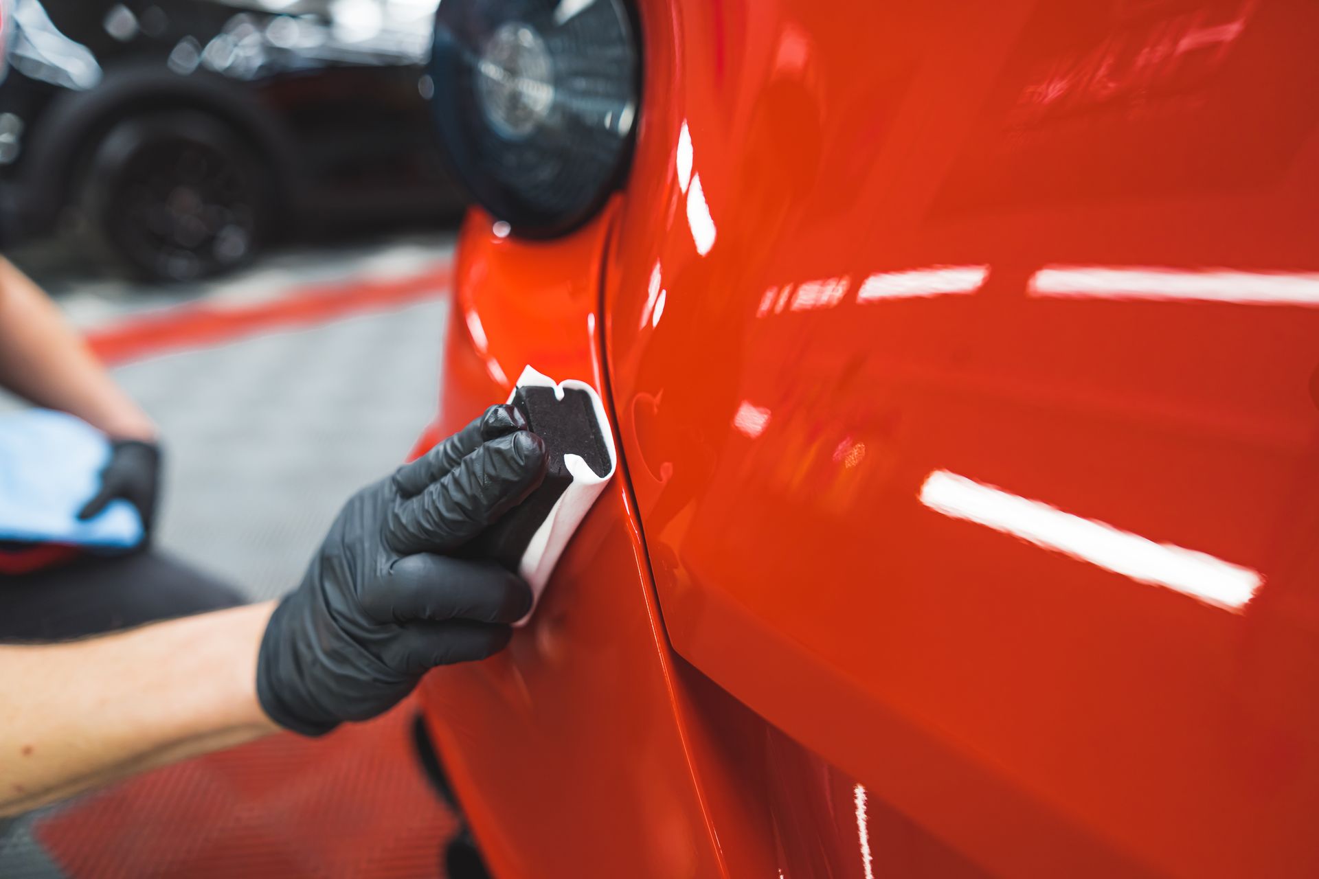 Gloved hand applying ceramic coating to a bright red car panel in a garage.