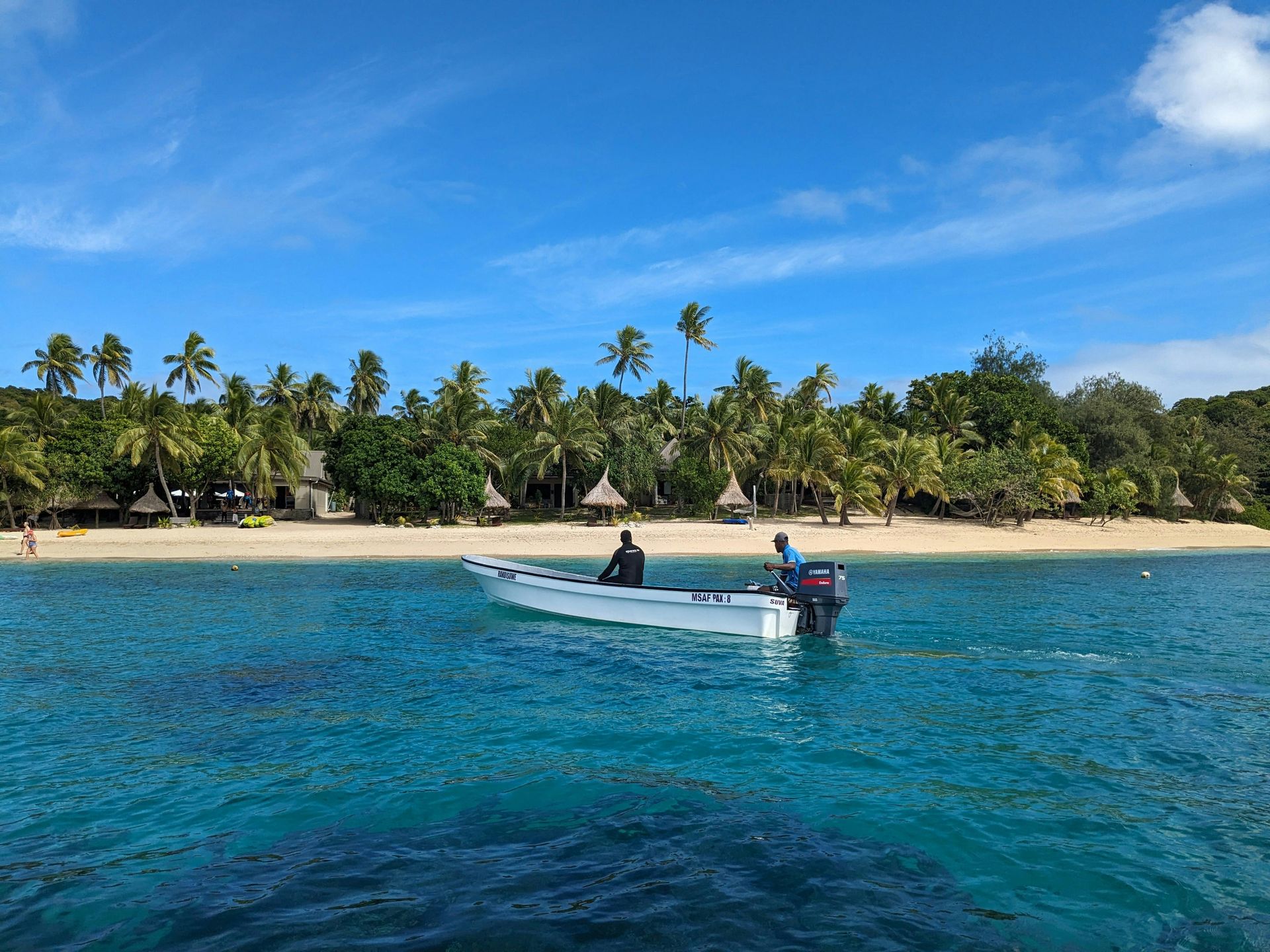 Small boat on clear blue water near a tropical beach lined with palm trees