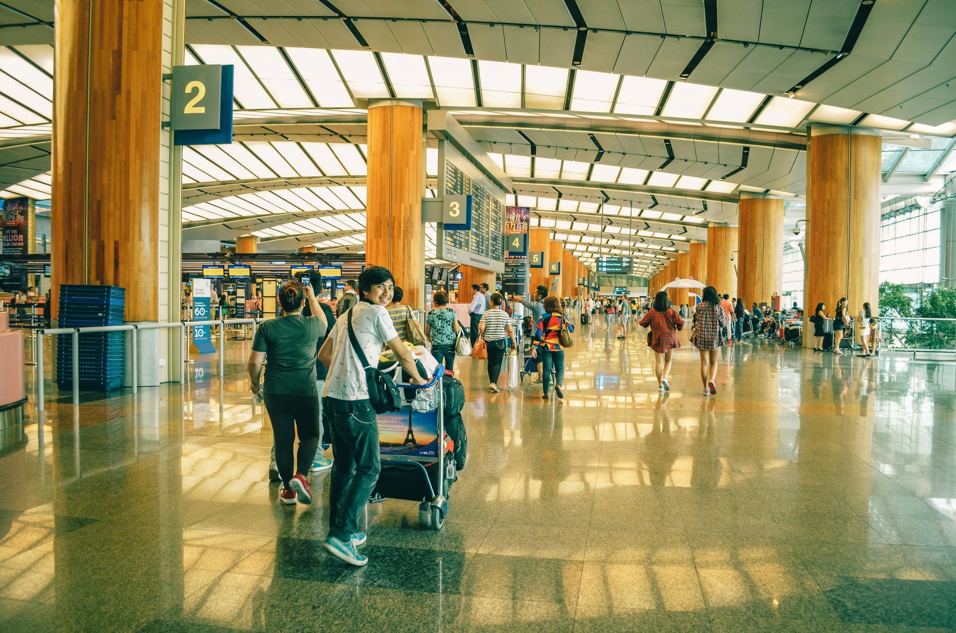 Airport terminal with people, shiny floor, tall wooden pillars, and signage.
