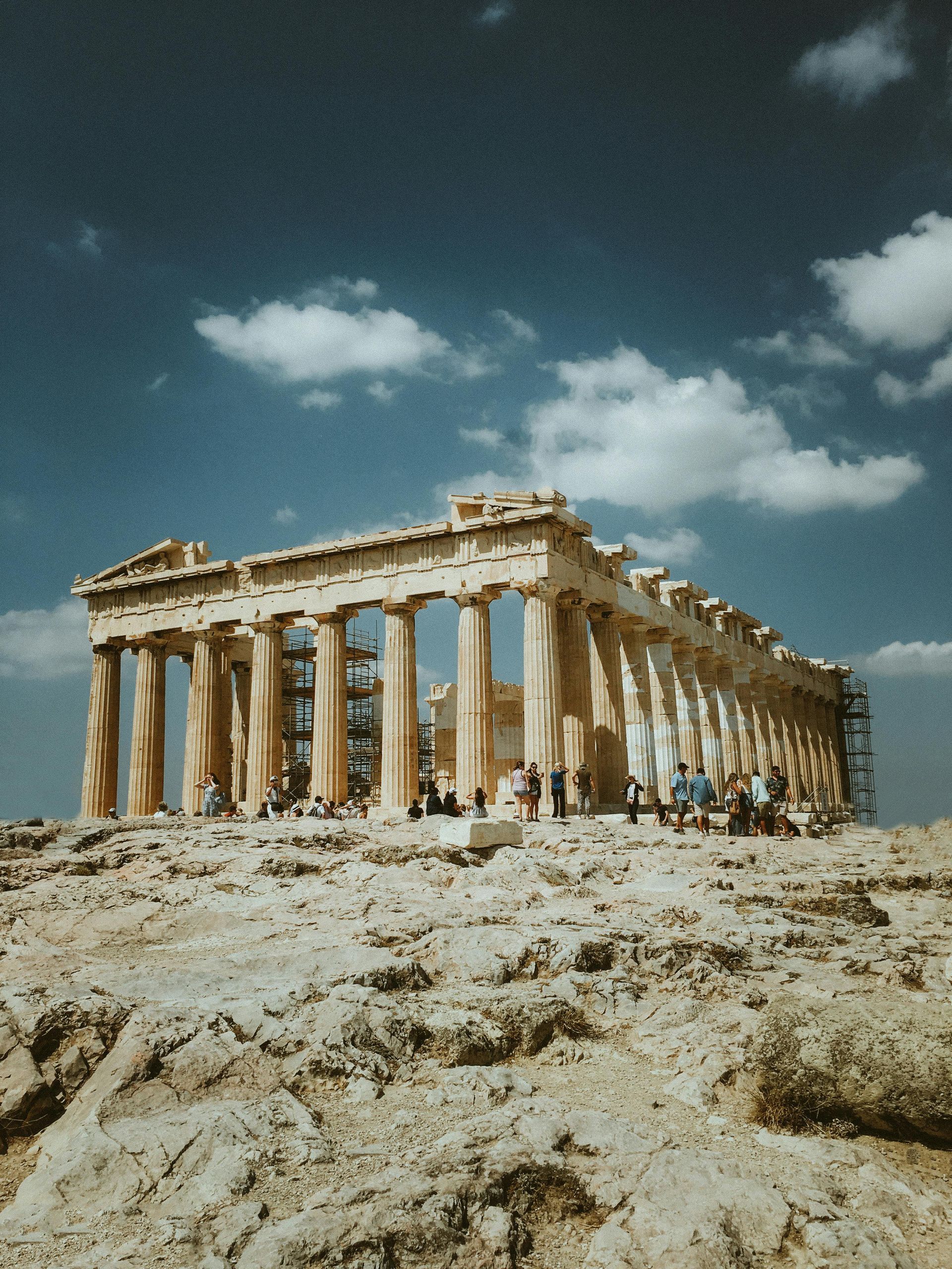 Ancient Greek temple ruins on a rocky hill under a blue sky with scattered clouds