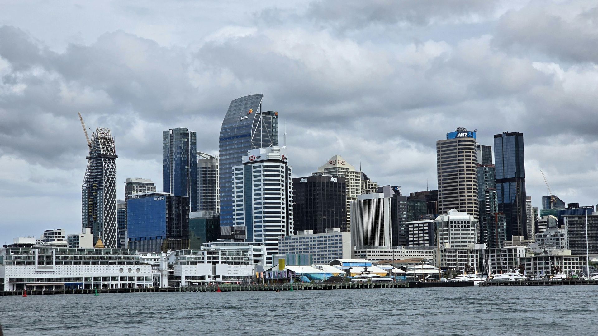 City skyline with modern high-rise buildings along a waterfront under a cloudy sky.