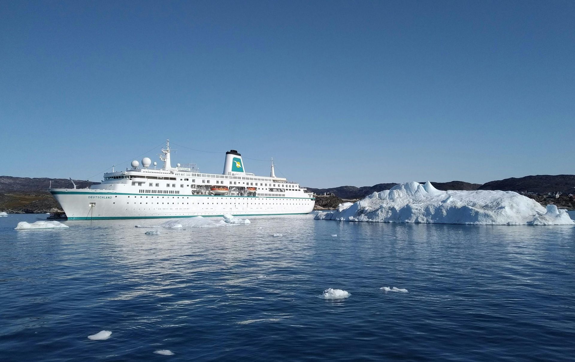 Cruise ship sailing near an iceberg in blue water under a clear sky.