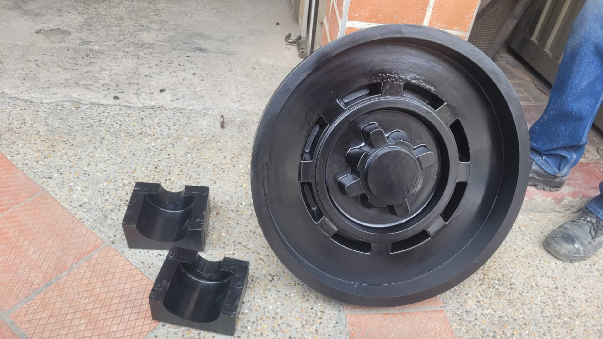 Una rueda negra junto a dos bloques negros en forma de U sobre una superficie de hormigón. Se ve una persona.
