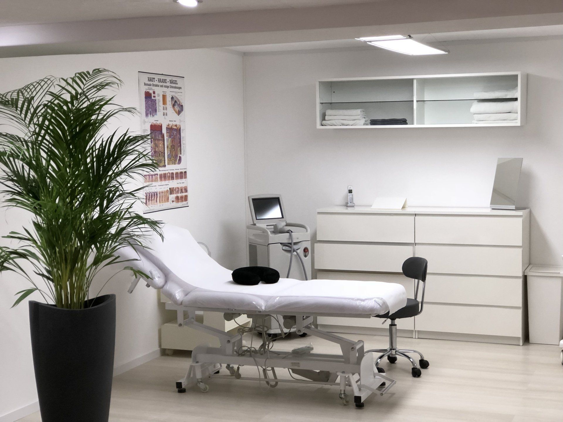 Eine Arztpraxis mit Bett, Stuhl, Kommode und Pflanze.