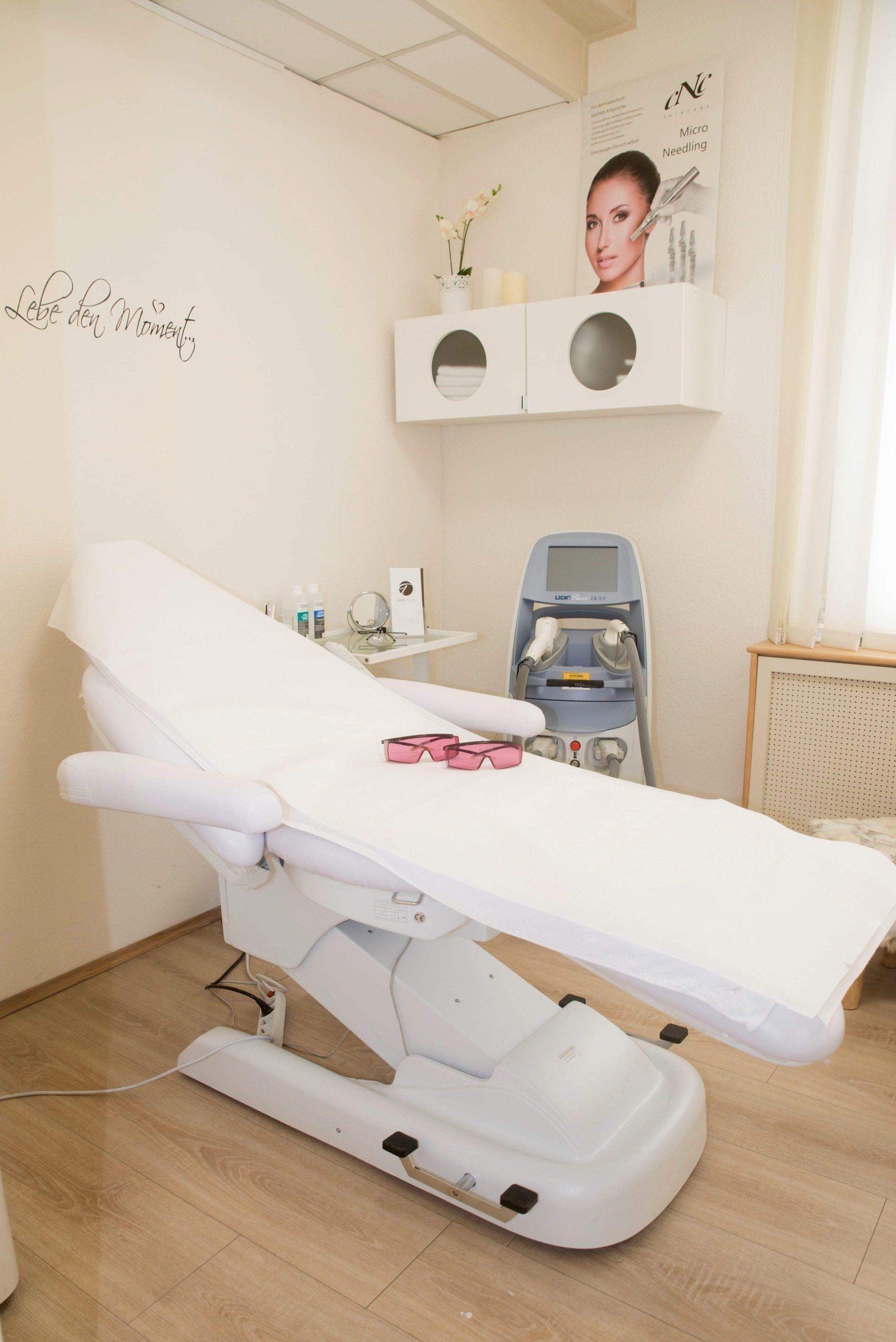 Ein weißer Massagetisch in einem Raum mit einem Frauenbild an der Wand.