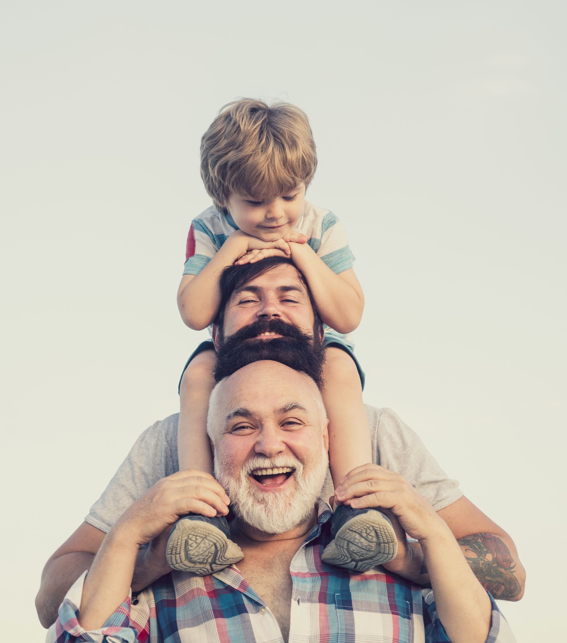 A man is carrying a little boy on his shoulders. Three generations of men with heads stacked vertically.