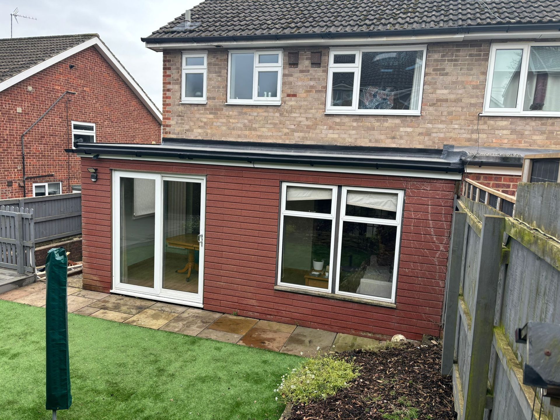 A two-story brick house with a ground-floor flat-roofed red brick extension featuring a sliding door and two windows.