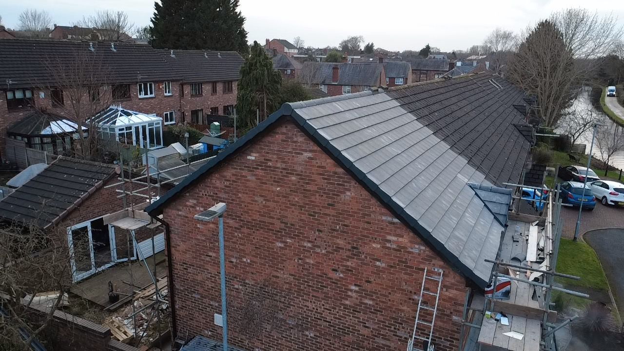 An elevated view of a brick house with a newly tiled roof, scaffolding, and surrounding homes in a residential area.