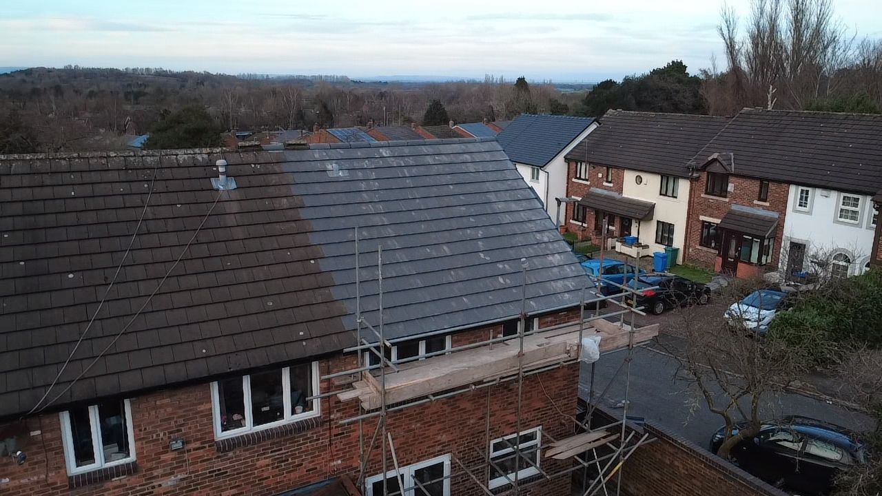 An aerial view shows a partially reroofed brick house with new dark gray tiles on one side and old, weathered tiles on left.