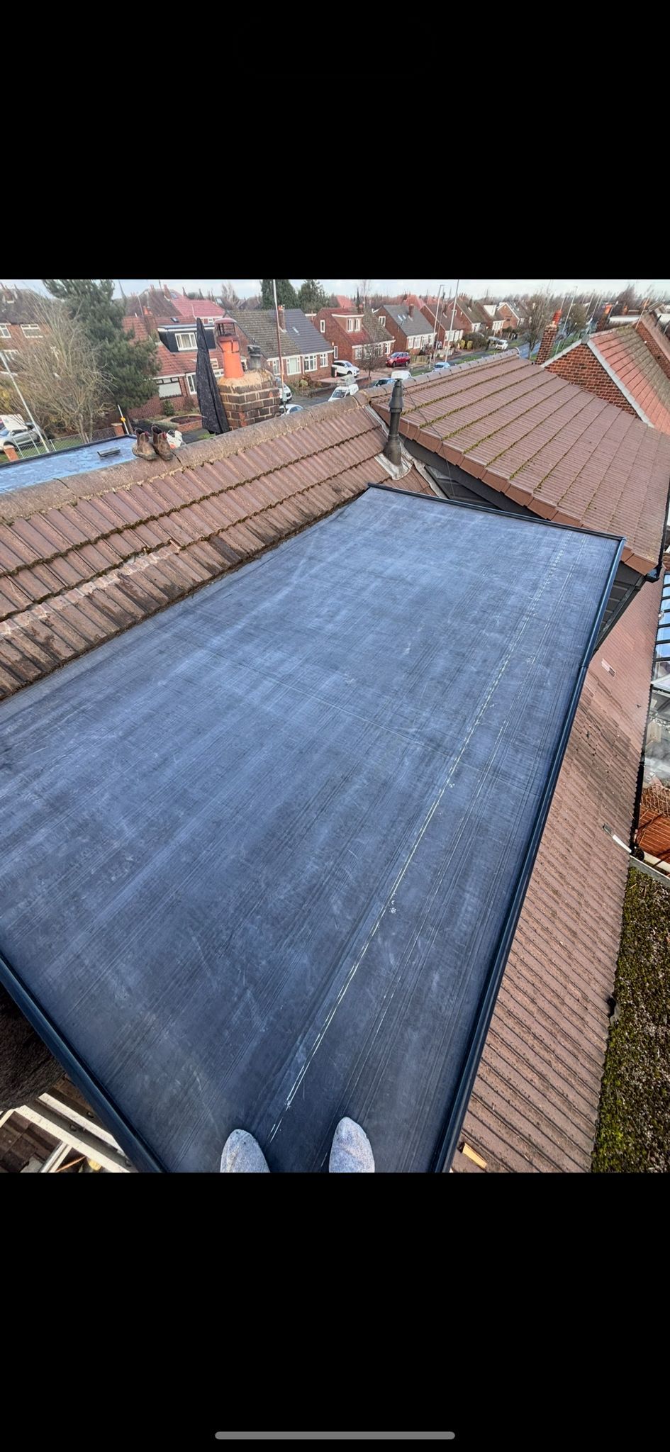 A large blue rectangular mat spread across a pitched, brown tiled roof, viewed from above.
