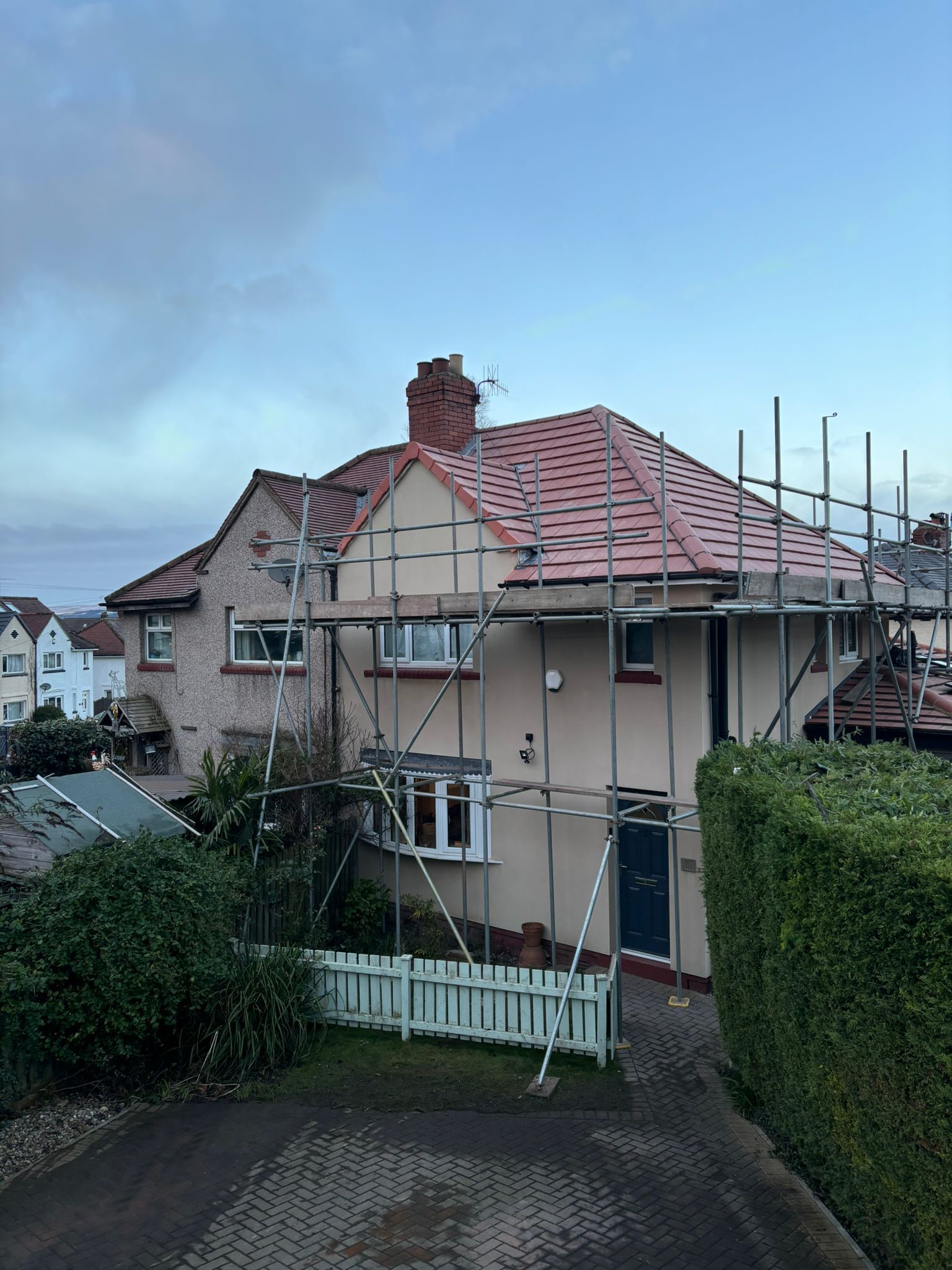 A two-story house under renovation, featuring scaffolding surrounding the exterior and a partially tiled roof.