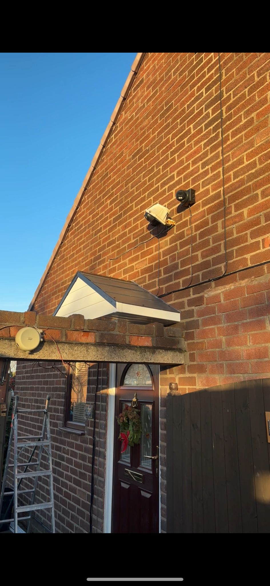 A low-angle view of a brick house exterior featuring a front door under a small canopy and a security light on the wall.