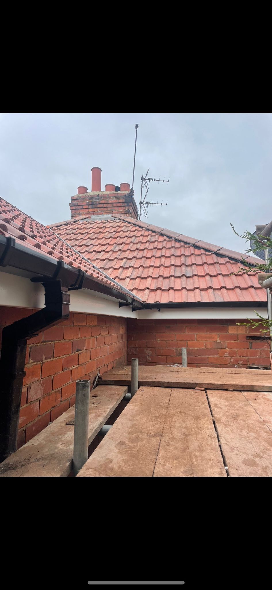 A view from a loft space showing a red-tiled roof, a brick chimney, and attic insulation between wooden beams.