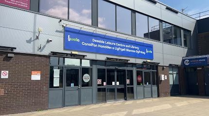 Exterior of a hospital entrance with a blue sign and glass doors under a cloudy sky