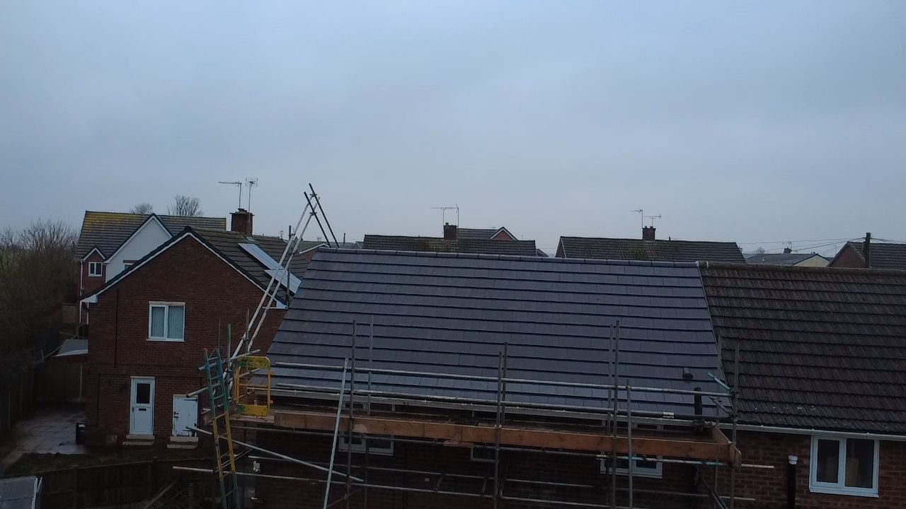 A house under renovation with scaffolding and a newly tiled dark grey roof set against a cloudy sky.