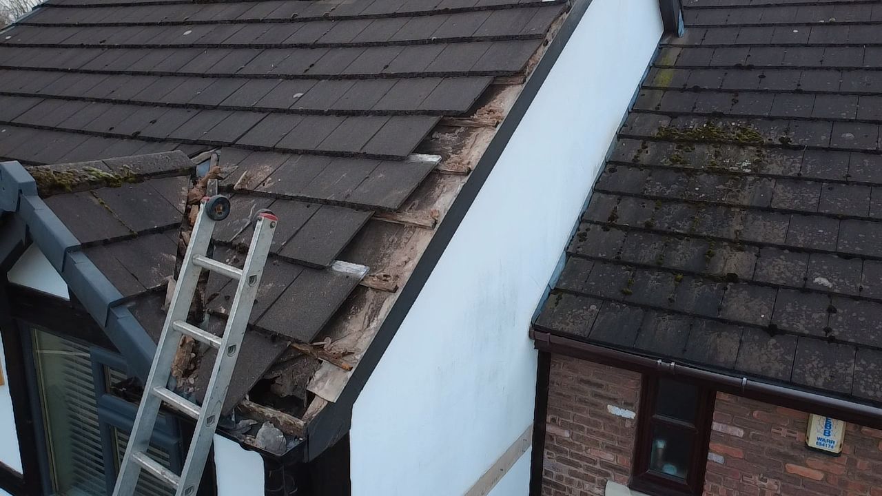 An aerial view of a residential roof showing damaged, missing tiles along the edge where it meets a white wall.
