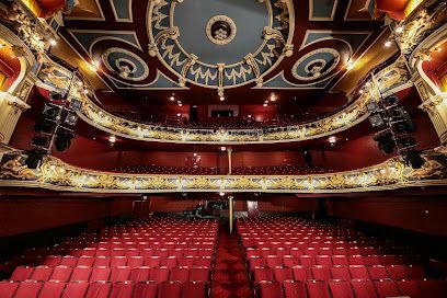 Empty ornate theater with red seats and gold trim, viewed from the stage toward the balcony.