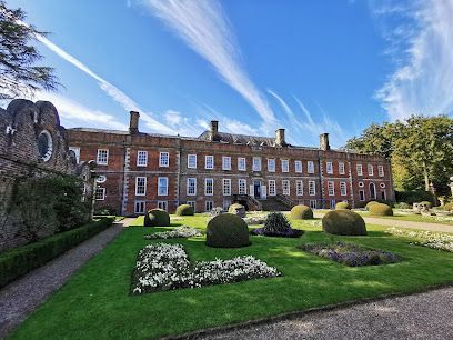 Historic brick building with a manicured garden, flower beds, and blue sky with wispy clouds.