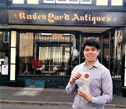 Person holding a book outside a storefront labeled “Raven Gard Antiques.”