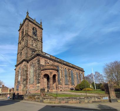 Stone church with a tall tower on a sunny day, viewed from the street with trees and blue sky
