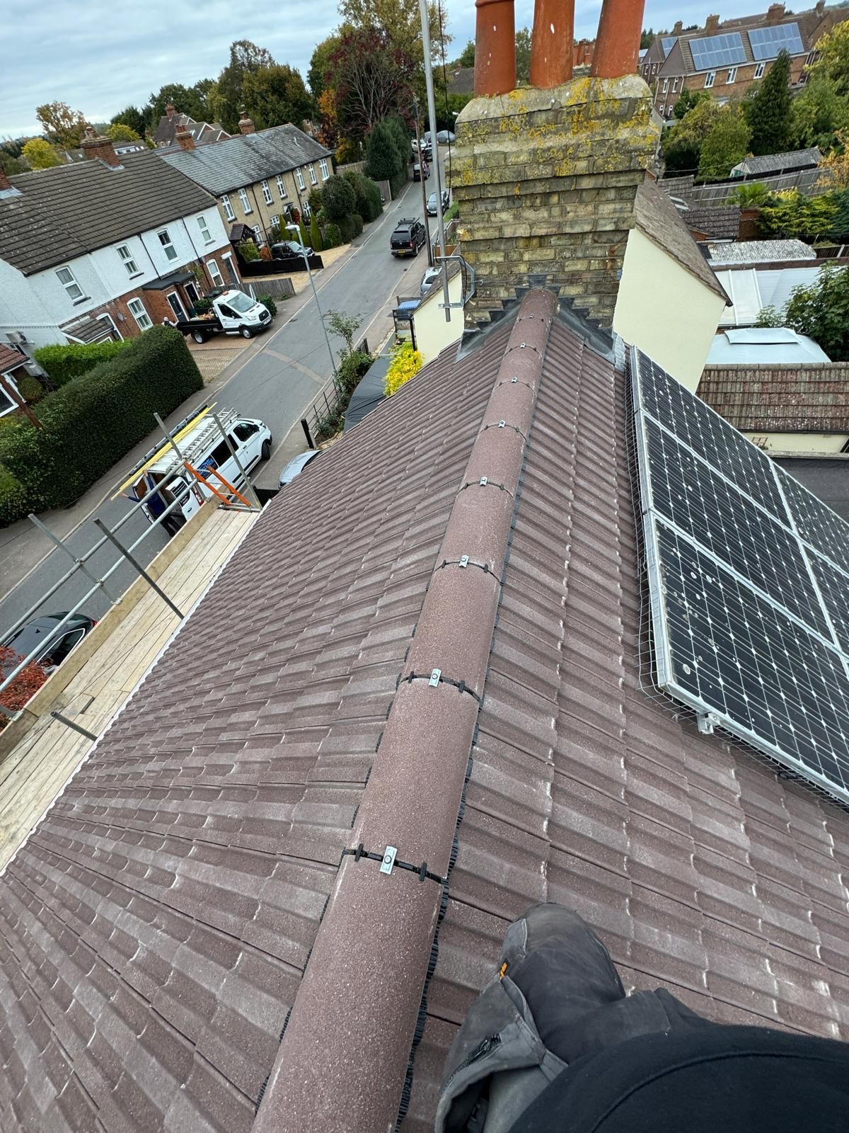 High-angle view of a tiled roof ridge with solar panels on the right, overlooking a street with parked vehicles.