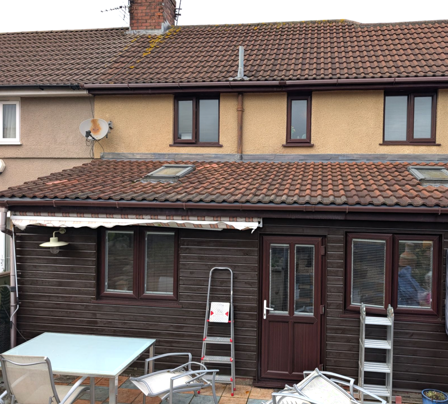 Backyard patio with dark wood extension, ladders, and outdoor furniture beneath a tiled roof