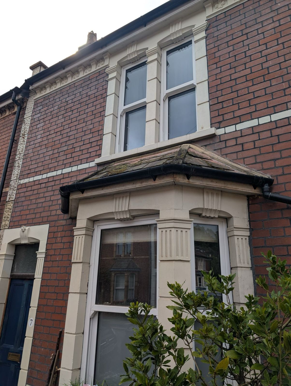 Brick terraced house facade with bay window and white-framed upper windows