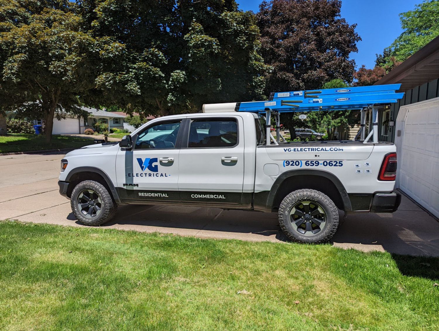 A white truck with a ladder on the back is parked in a driveway.
