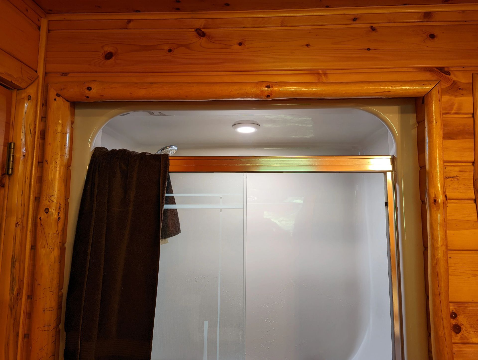 A bathroom in a log cabin with a shower and a towel hanging on the door.