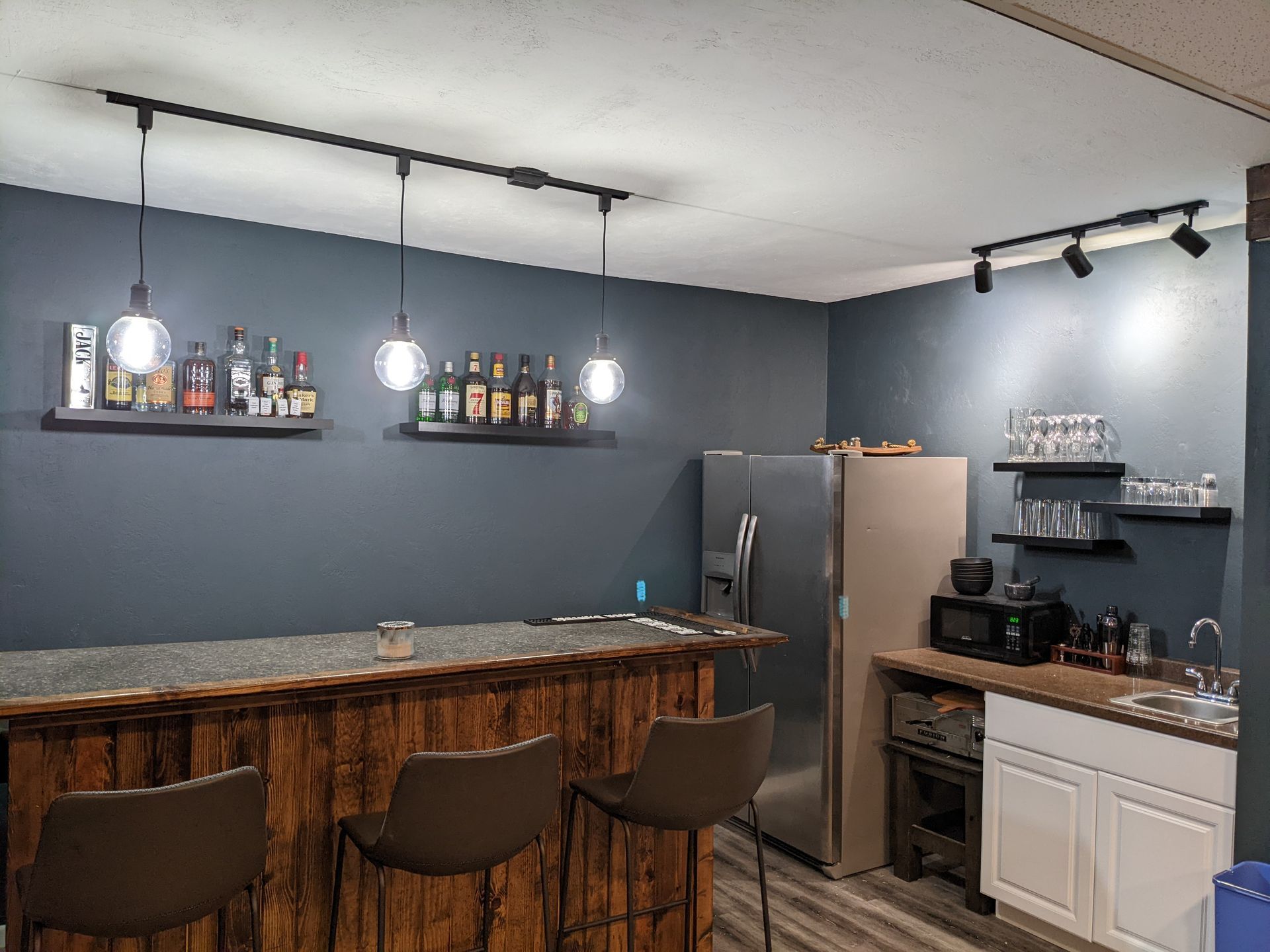 A kitchen with a bar and stools and a refrigerator.