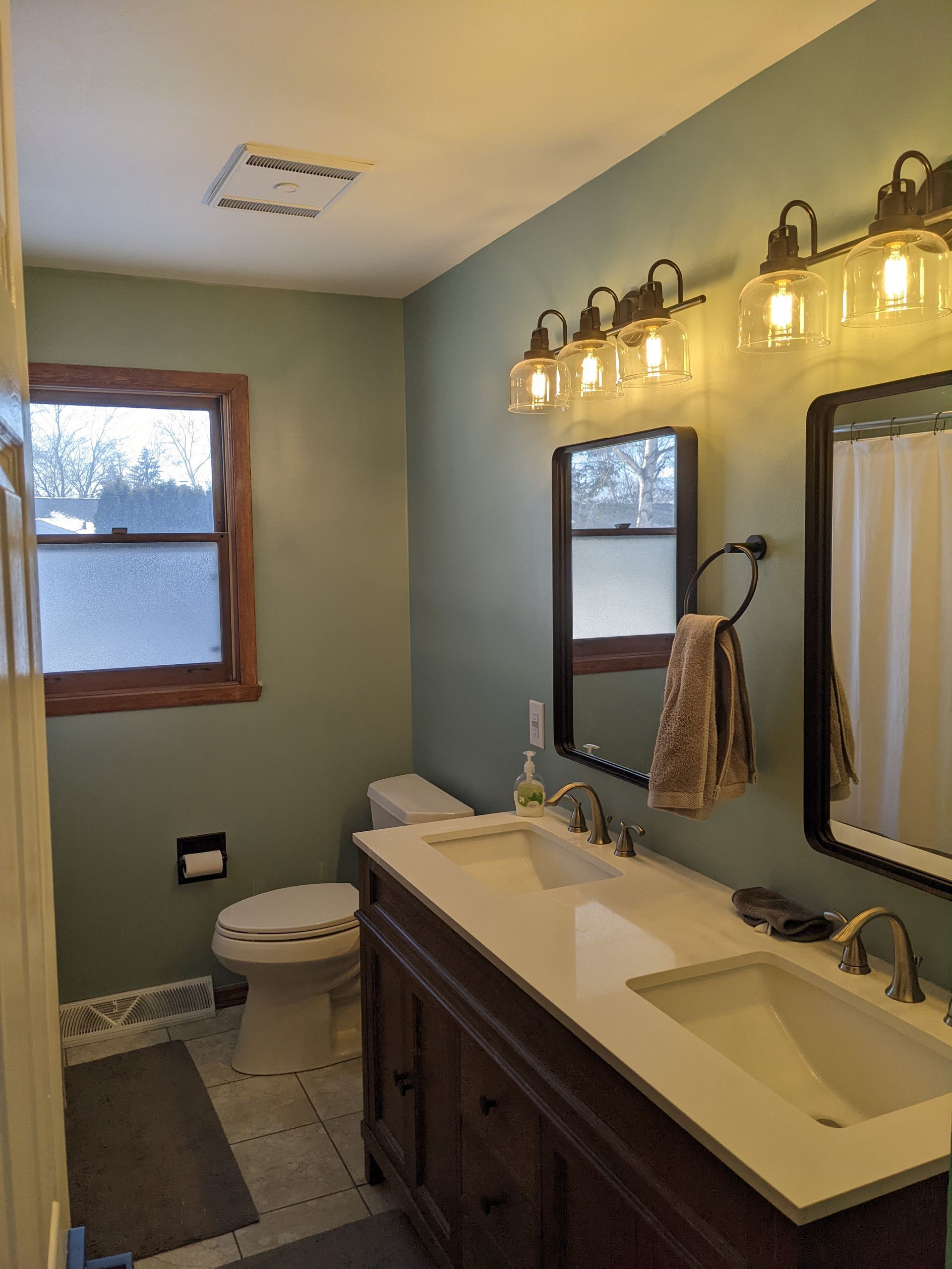 A bathroom with a toilet , sink , mirror and window