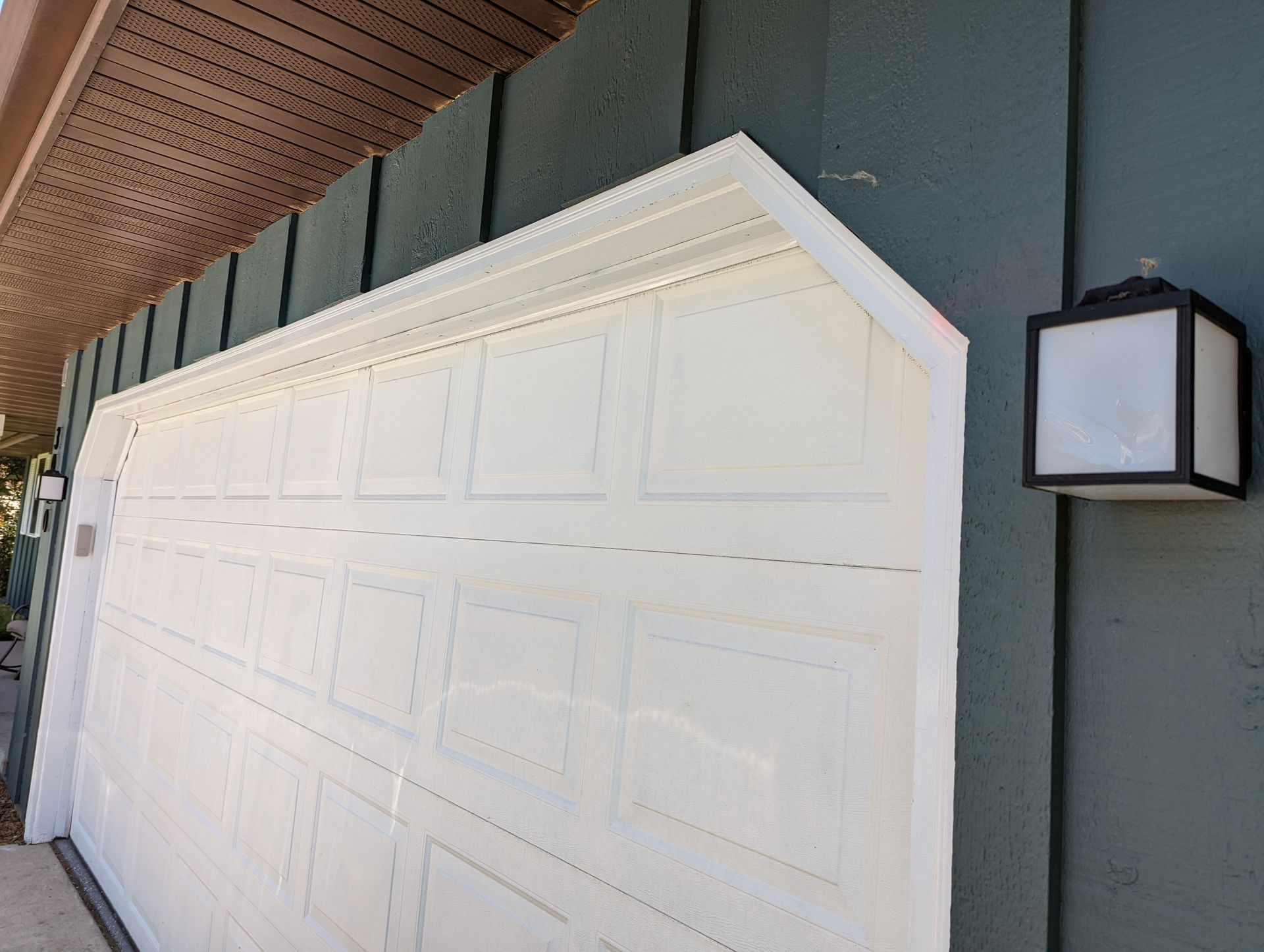 A white garage door is open on the side of a house.