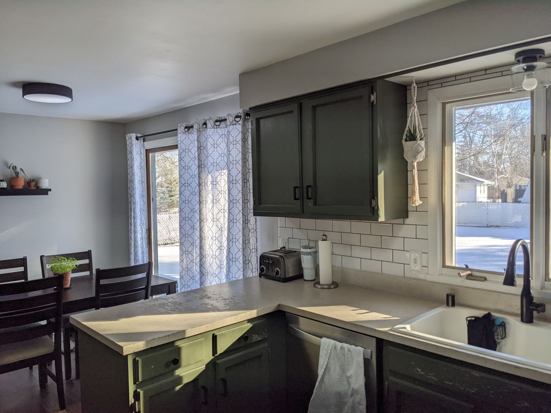 A kitchen with green cabinets , a sink , a table and chairs.