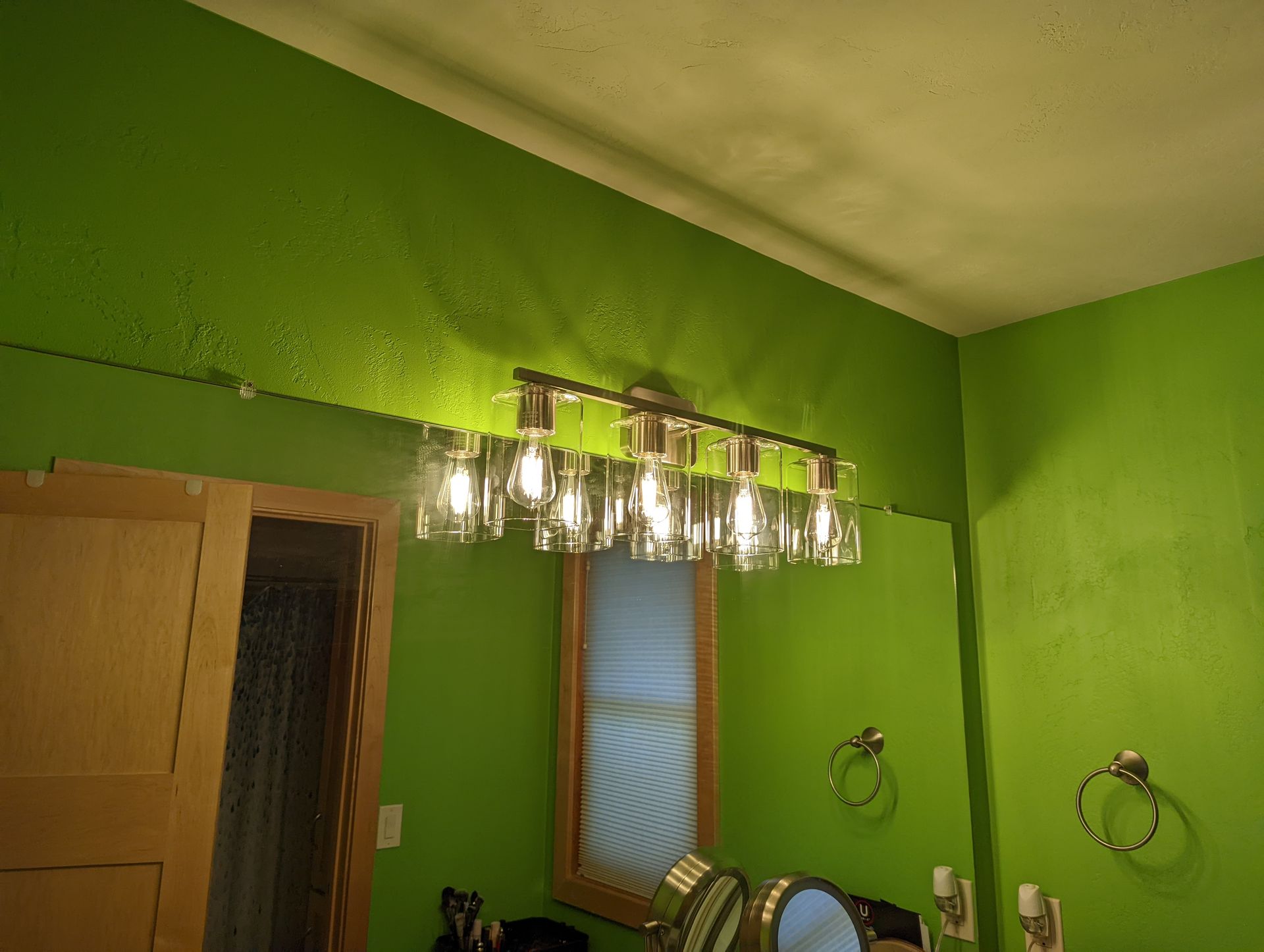 A bathroom with green walls and a light fixture hanging from the ceiling.