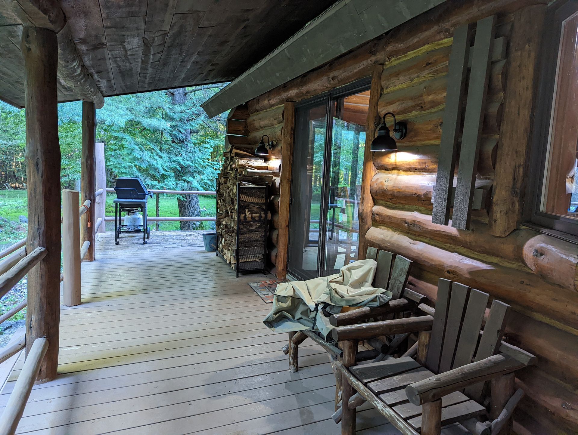 A log cabin with a porch with chairs and a grill.