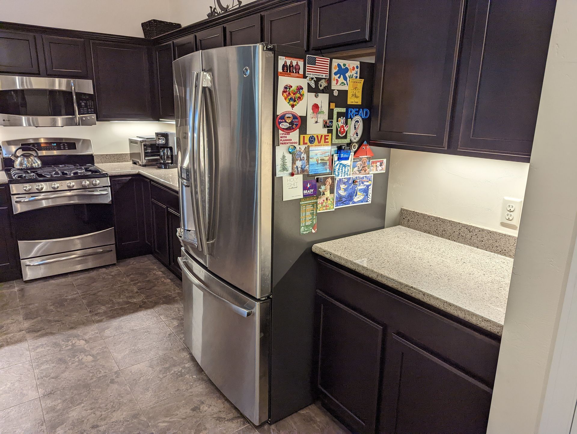 A kitchen with black cabinets and a stainless steel refrigerator
