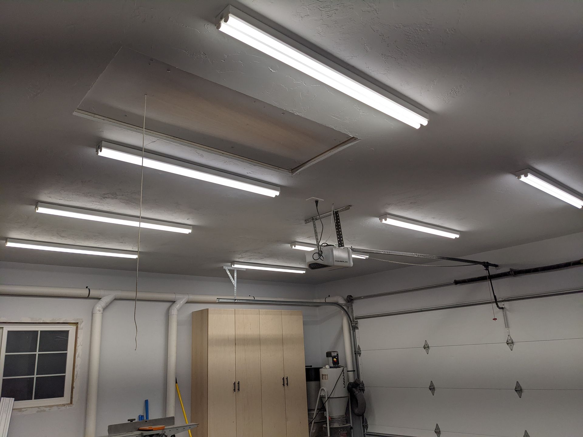 A garage with a lot of lights on the ceiling and a garage door open.