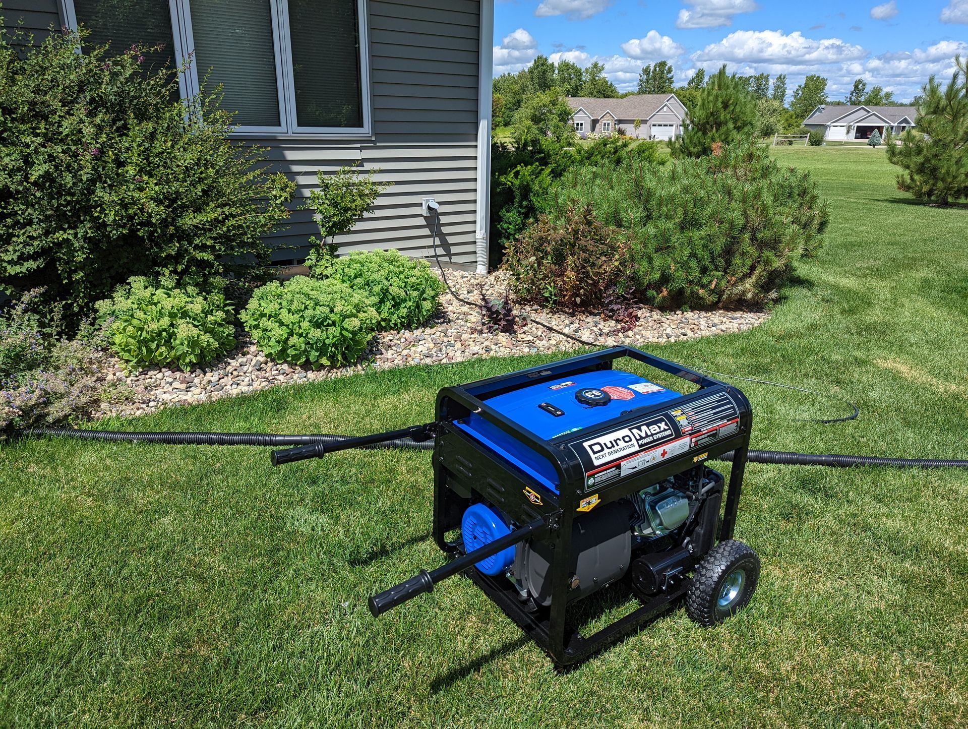 A generator is sitting in the grass in front of a house.