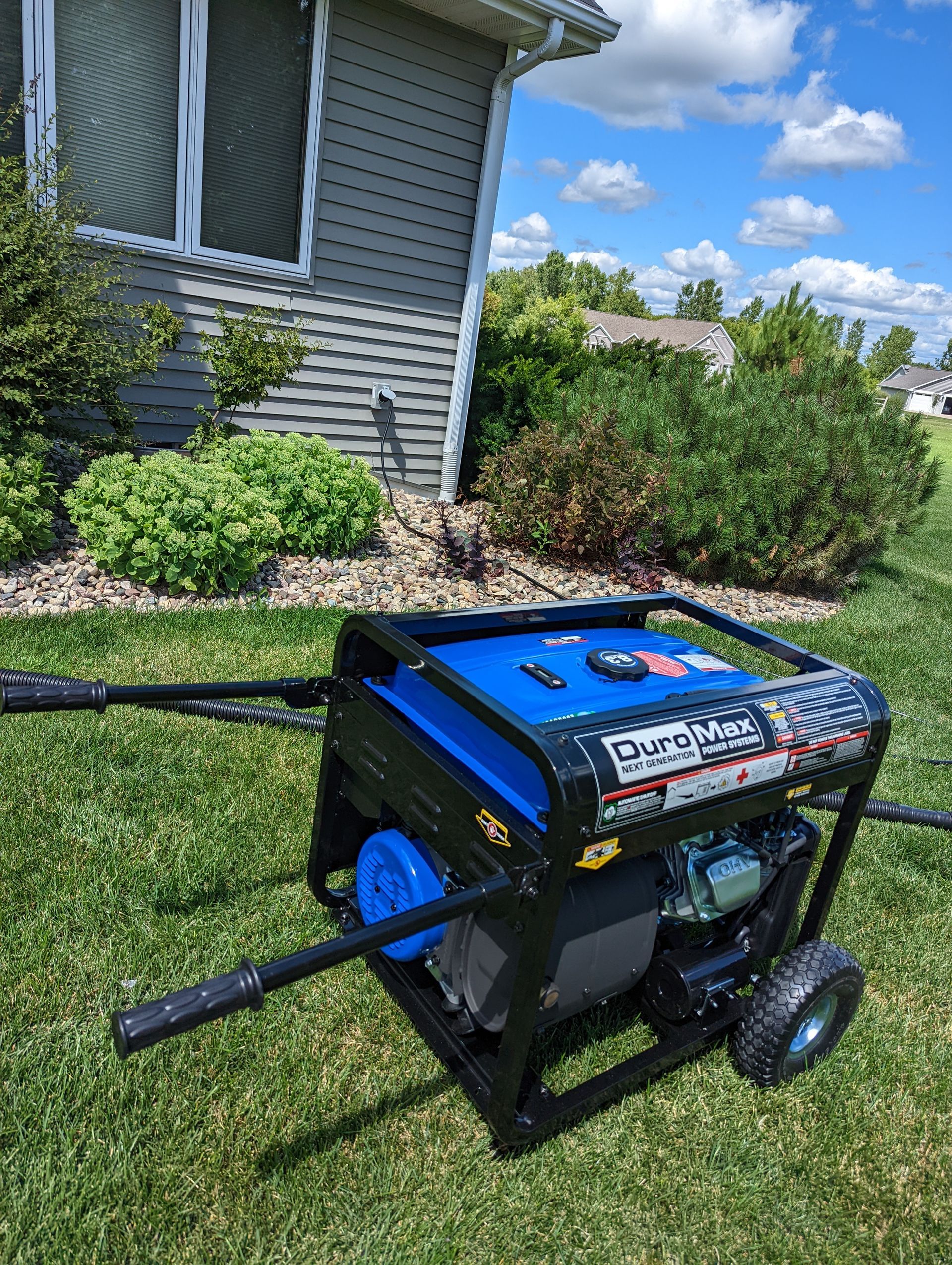A generator is sitting in the grass in front of a house.