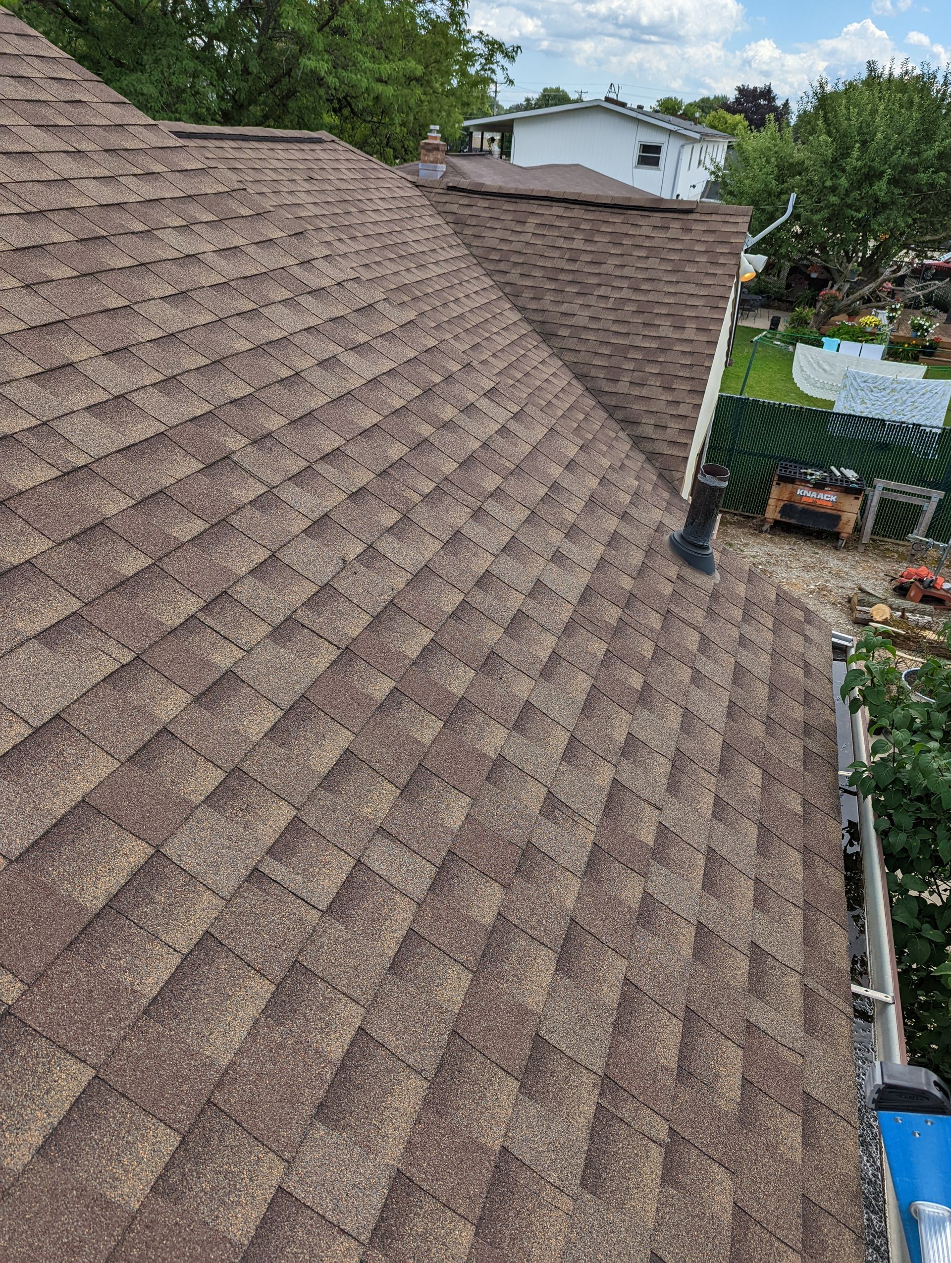A roof with a lot of shingles on it and a house in the background.