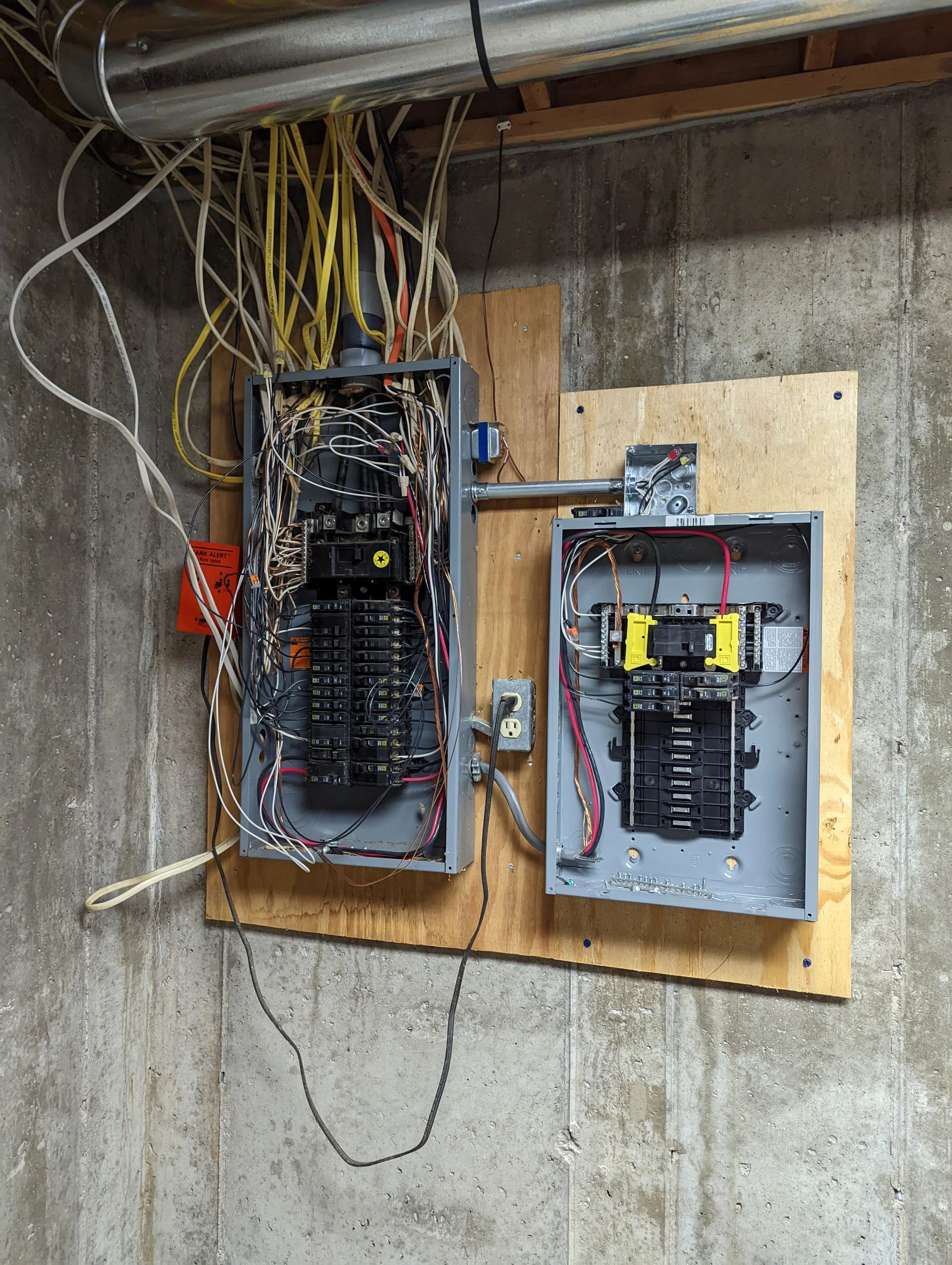 Two electrical boxes are hanging on a wooden board on a wall.