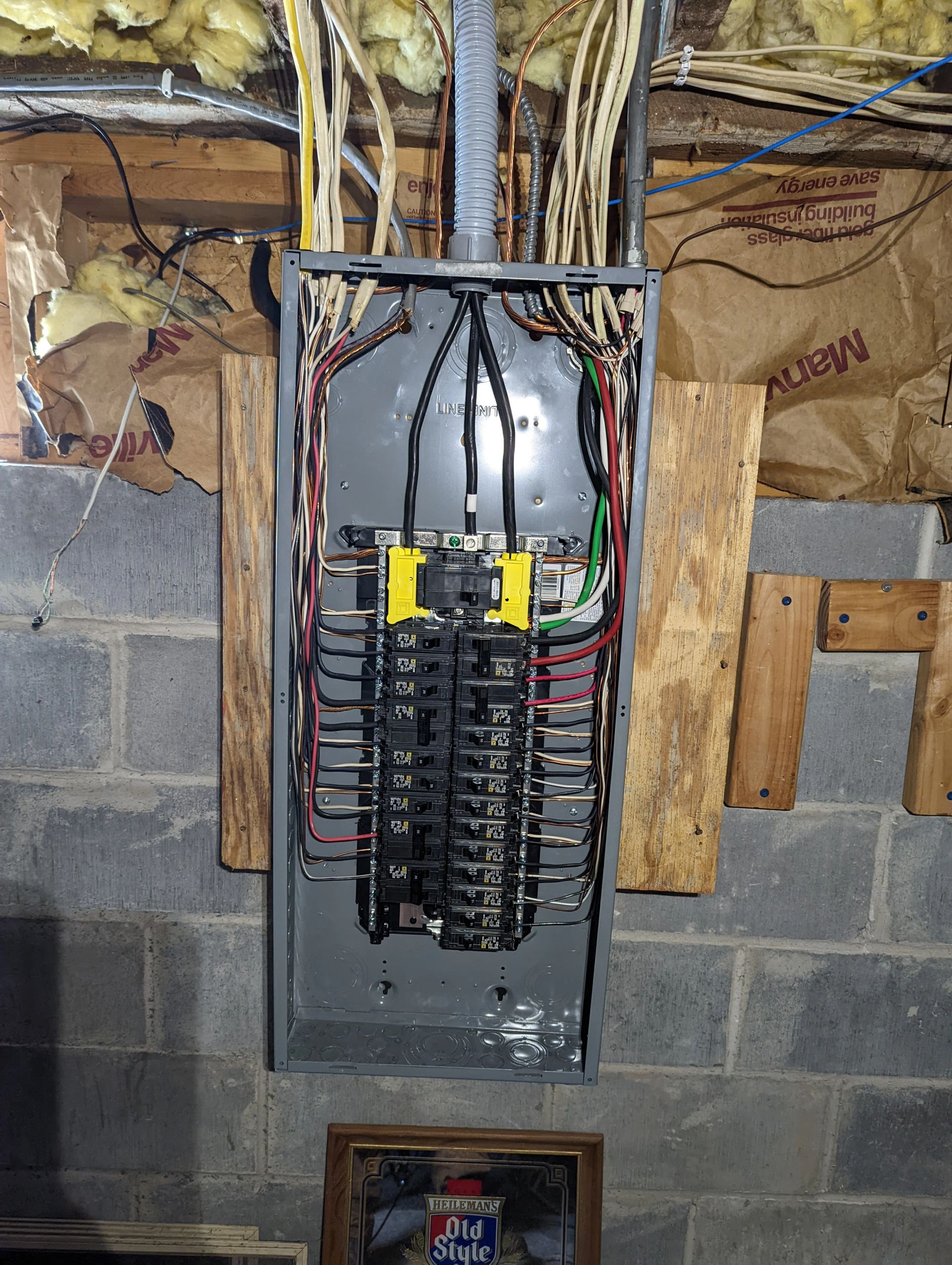 A electrical panel is hanging on a brick wall in a basement.