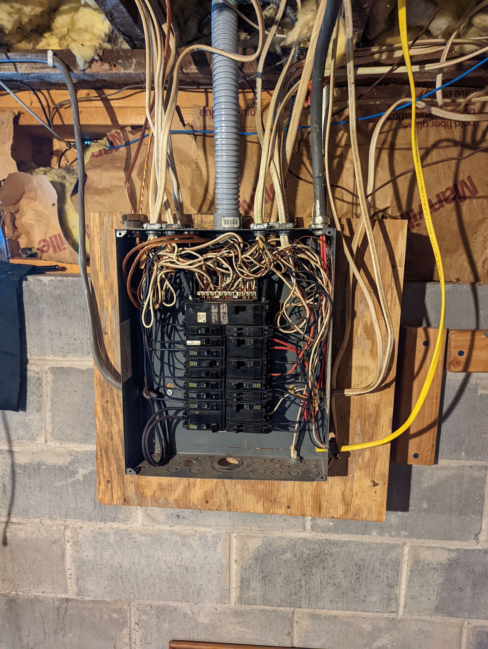 A very messy electrical box is hanging on a brick wall.