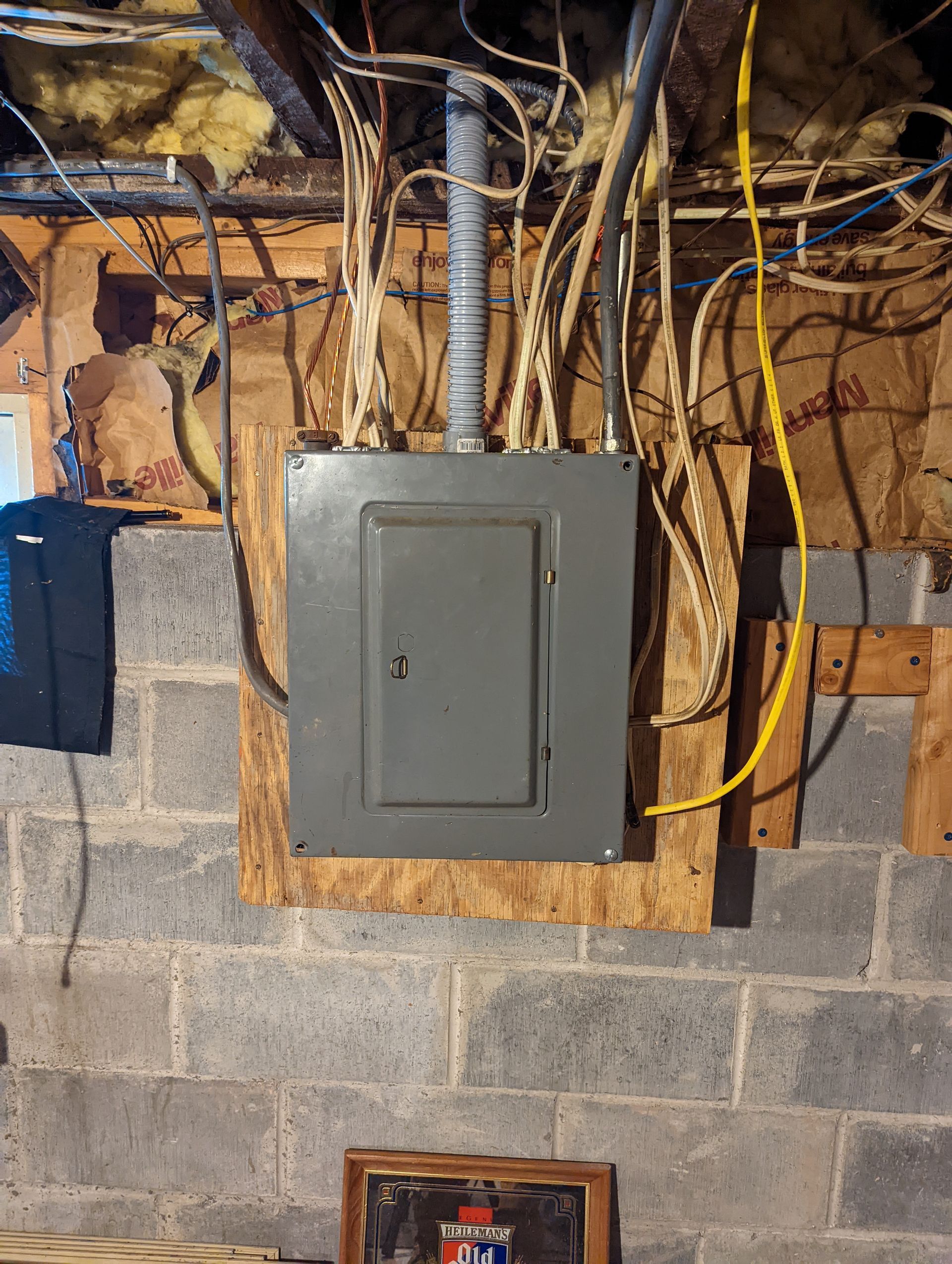 An electrical box is mounted on a brick wall in a basement.