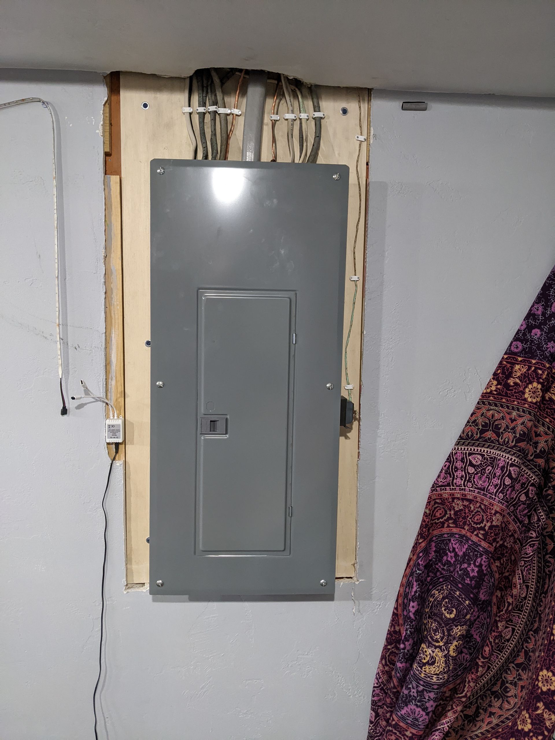 A gray electrical box is hanging on a wall next to a purple blanket.