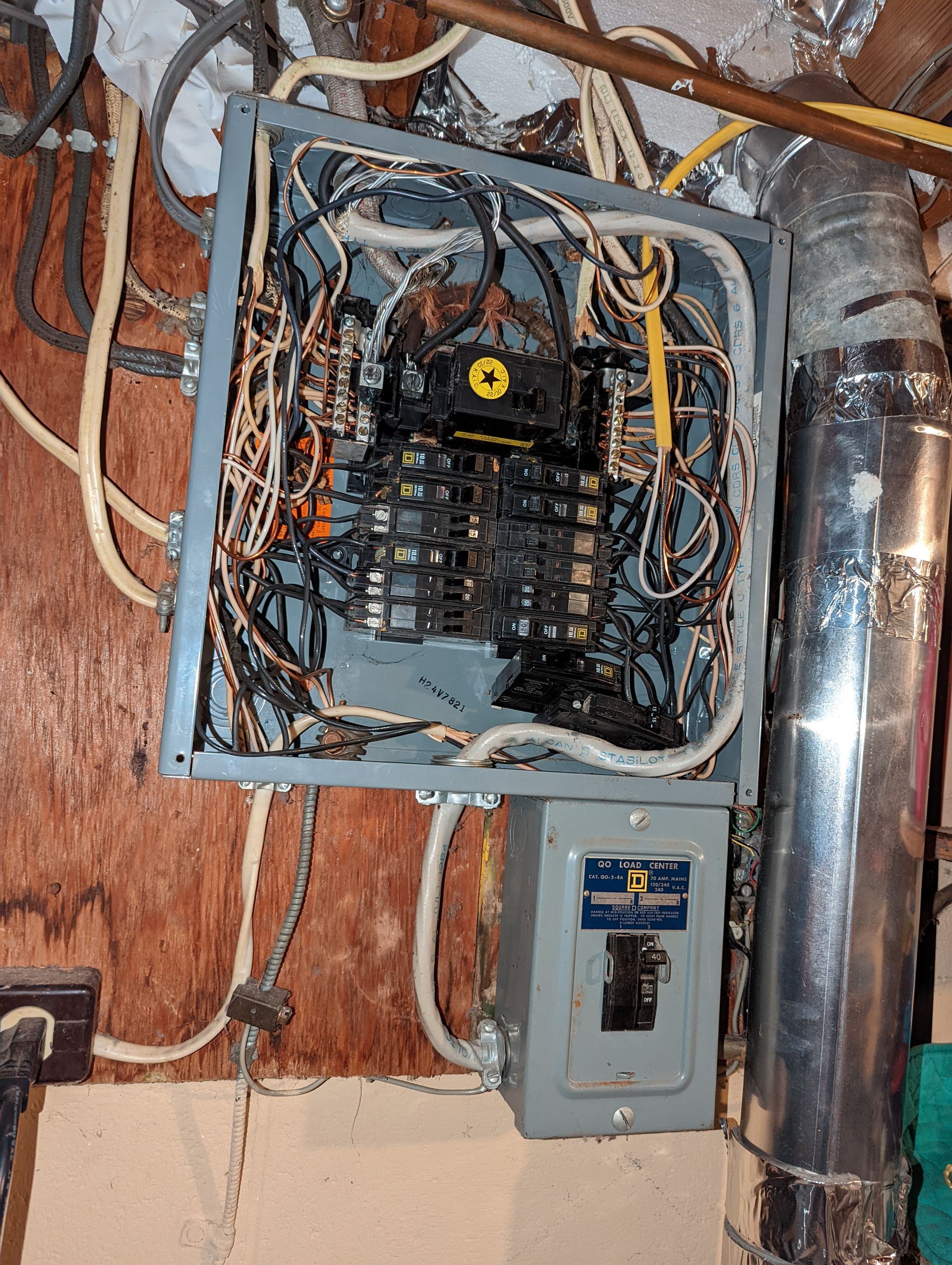 A very messy electrical box is sitting on a wooden wall.