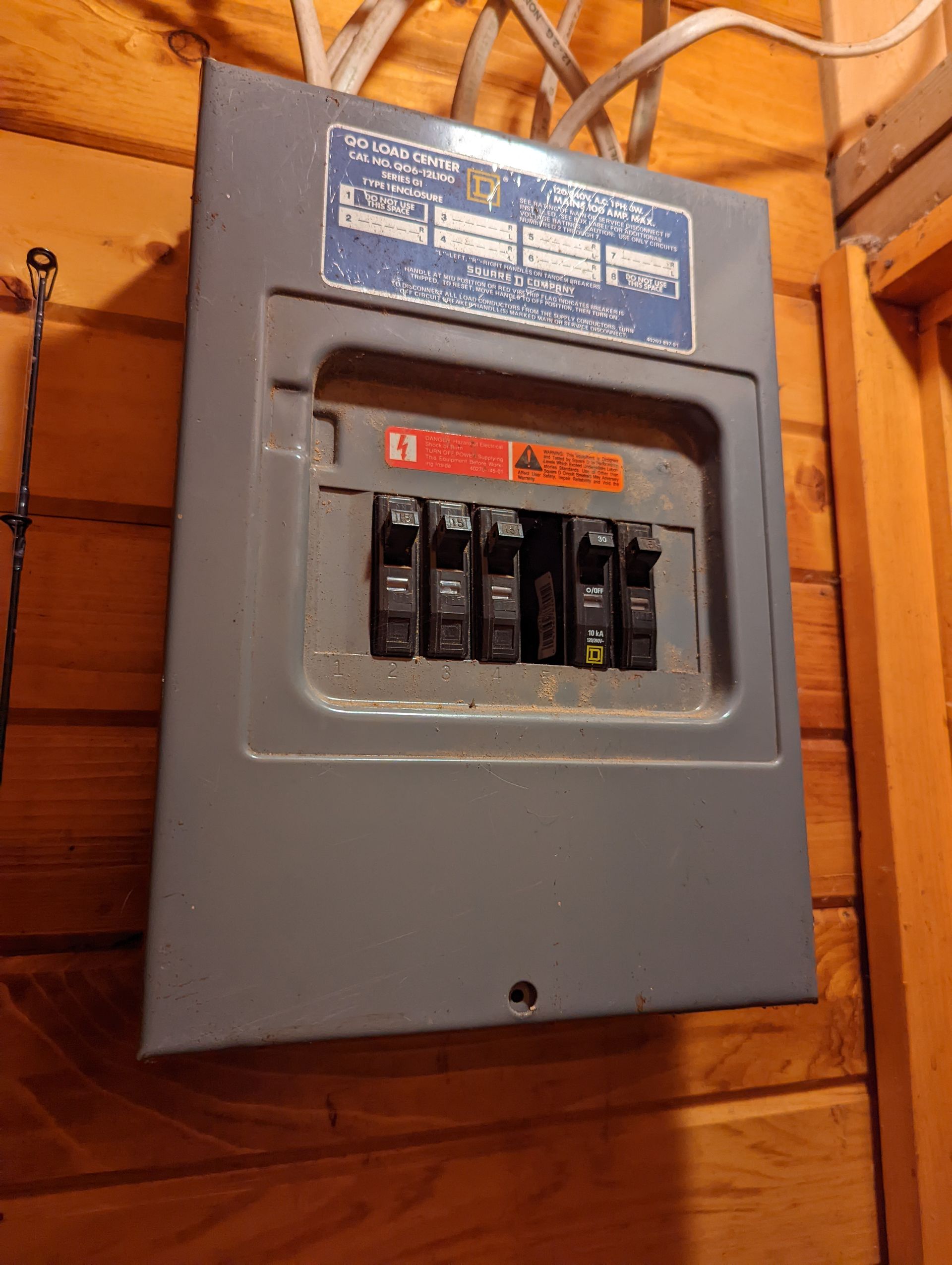 A electrical box is hanging on a wooden wall.